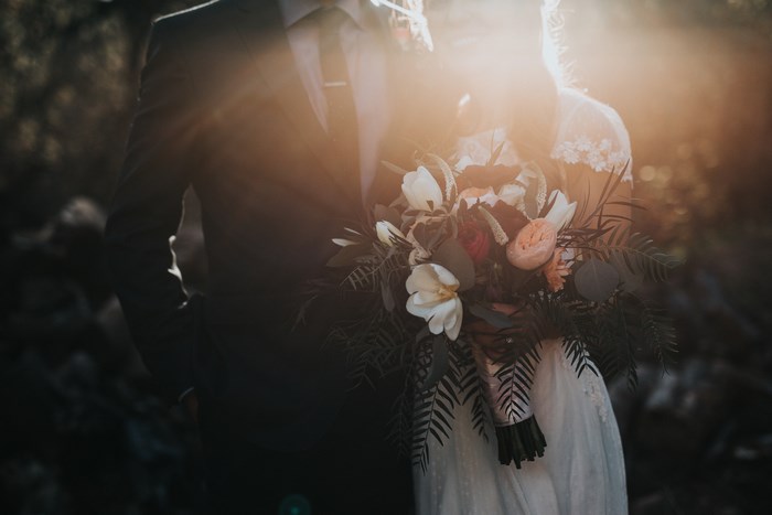 Wedding couple holding a bouquet in sunlight