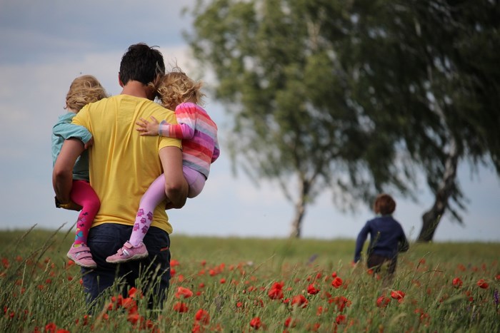 Father carrying two daughters in a poppy field