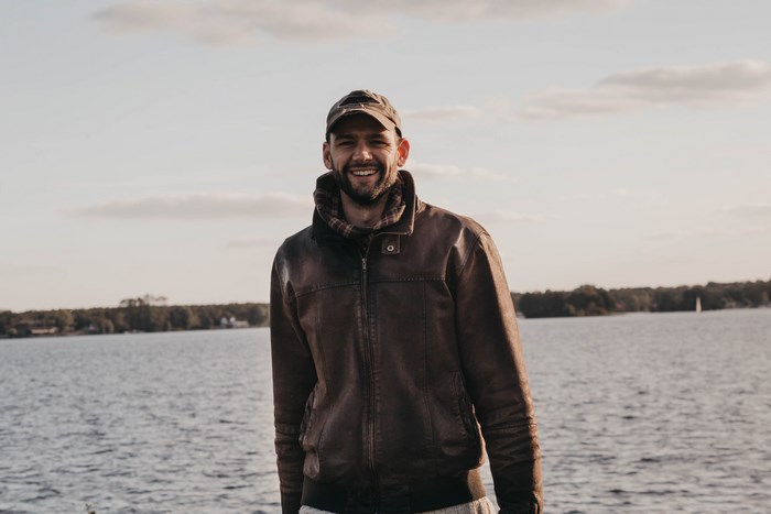Man in leather jacket and cap smiling by the water