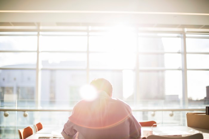 Man sitting at a table by a large window with sunflare
