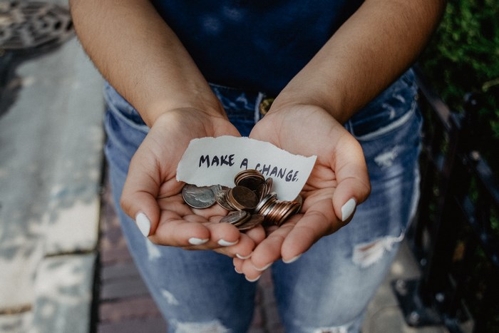 Person holding coins and a note that says "MAKE A CHANGE"
