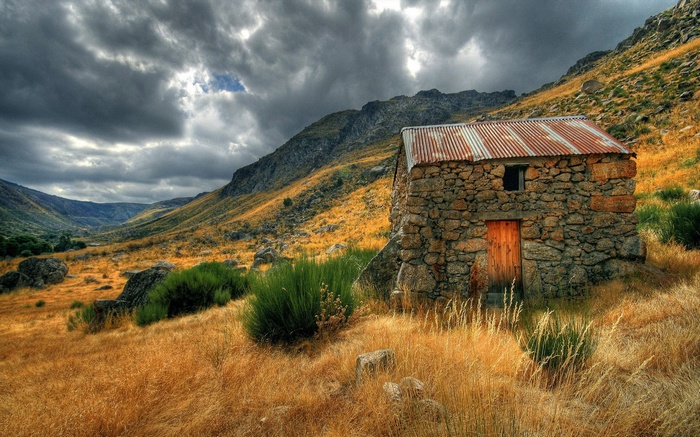 Stone cabin in a mountainous valley under stormy skies