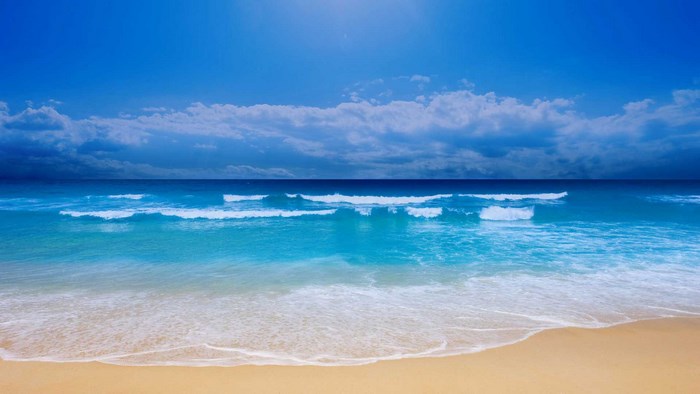 Ocean waves on a sandy beach under a blue sky