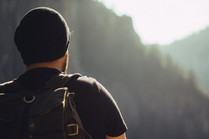 Man wearing a beanie and backpack looking at mountains