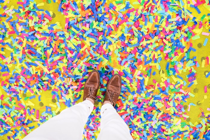 Man standing on colorful confetti with white pants and brown shoes