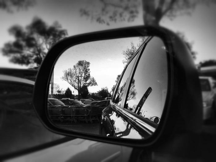 Car side mirror reflection of parking lot and trees
