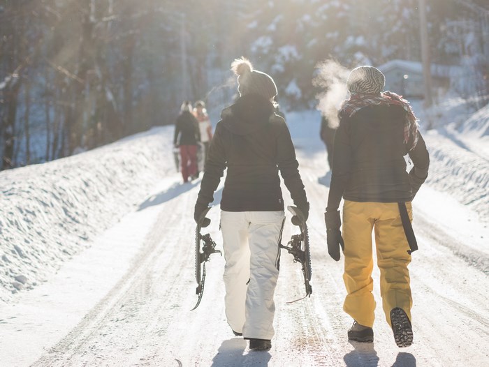 People walking on a snowy path with snowboards