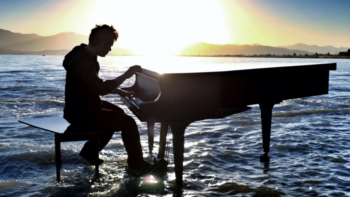 Man playing piano in water at sunset