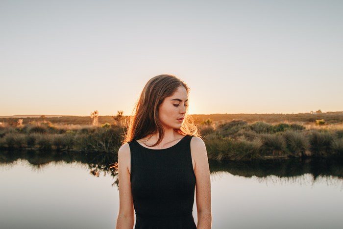 Woman in black dress by a lake at sunset