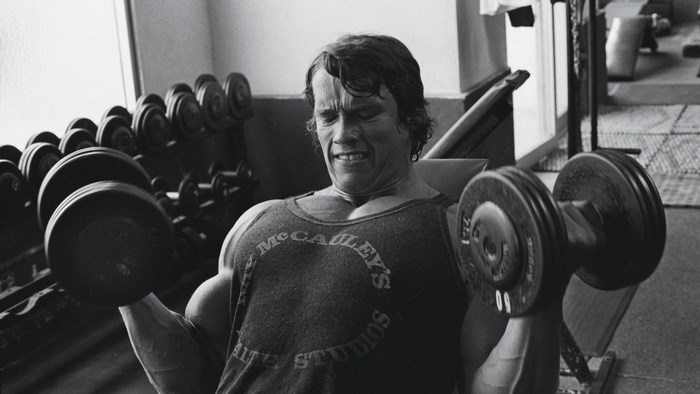 Arnold Schwarzenegger lifting dumbbells at McCauley's Studios