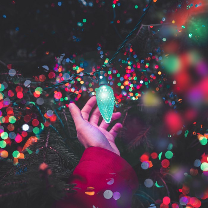 Hand reaching for a glowing Christmas light bulb