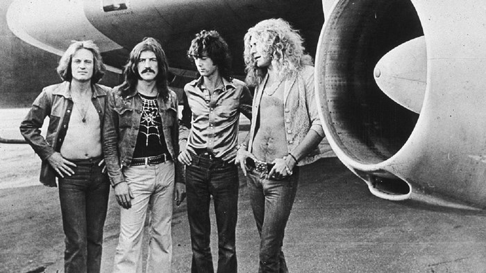 Led Zeppelin standing by an airplane engine
