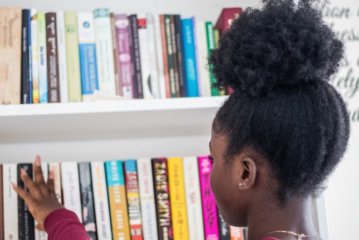 Black girl with afro reaching for books on a shelf