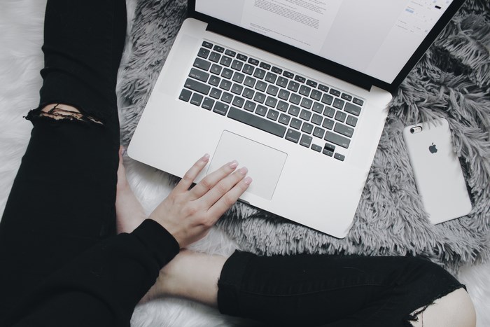 Person working on a MacBook with an iPhone on a rug