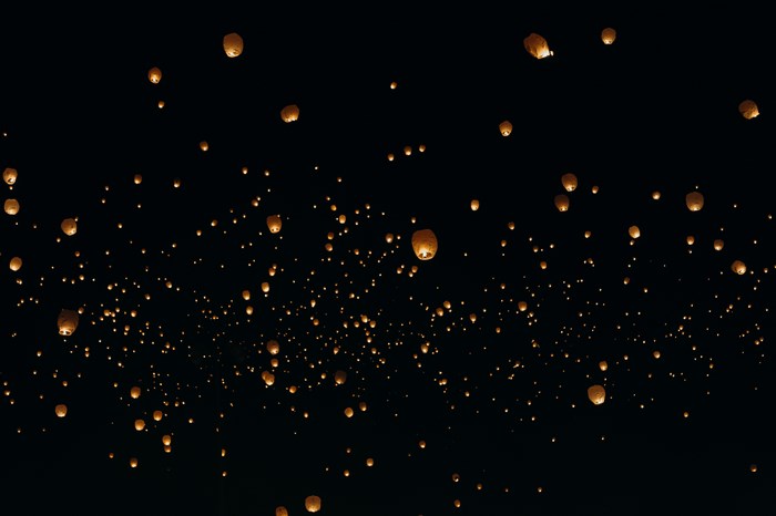 Many illuminated lanterns floating in the night sky