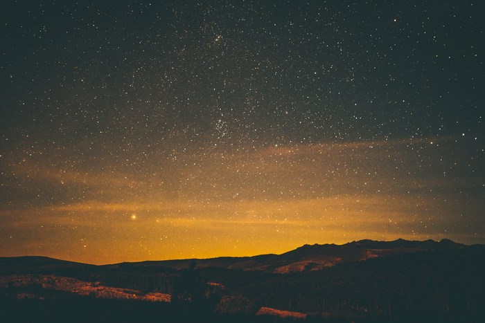 Starry night sky over mountains with orange glow
