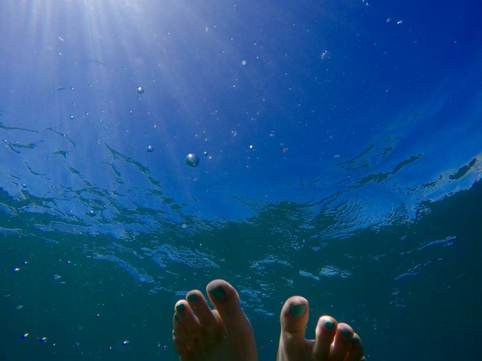 Feet underwater with sun rays and bubbles