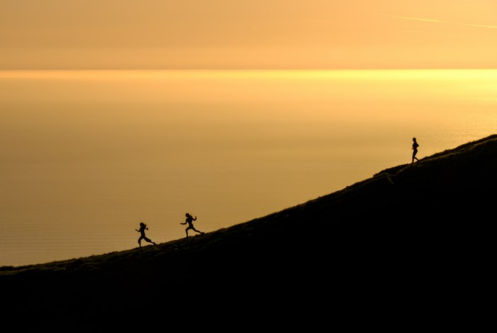 Three people running up a slope at sunset