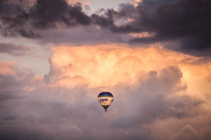 Hot air balloon floats among dramatic clouds at sunset