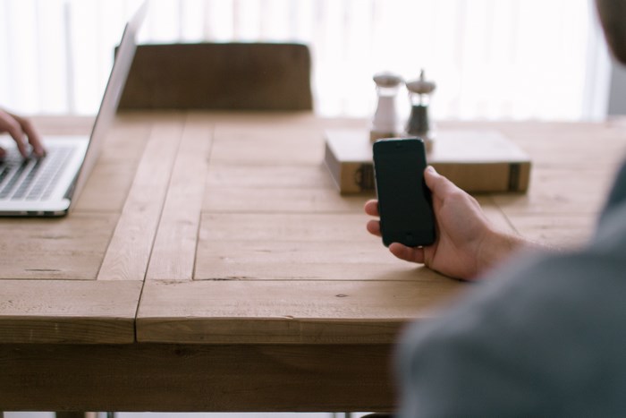 Person using iPhone and laptop on a wooden table
