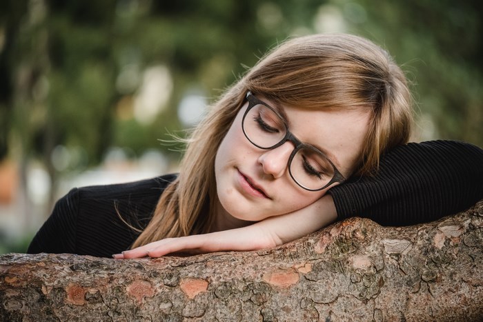 Young woman with glasses resting on a tree