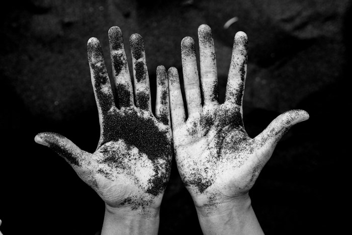 Black and white image of hands covered in sand