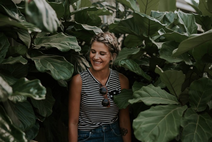 Woman with braided hair smiling among large green leaves