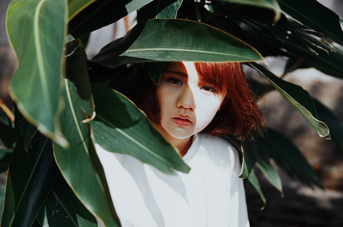 Asian woman hiding behind green foliage