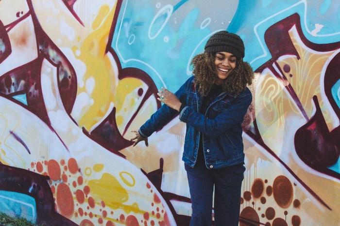 Woman in denim jacket dancing in front of graffiti art