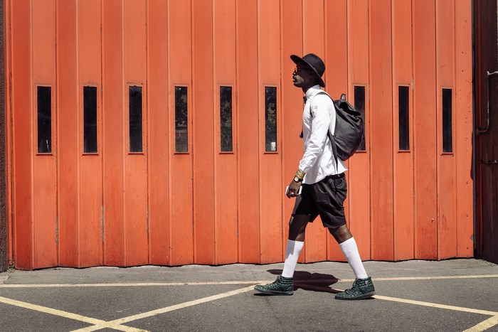 Man in hat and backpack walks by orange door