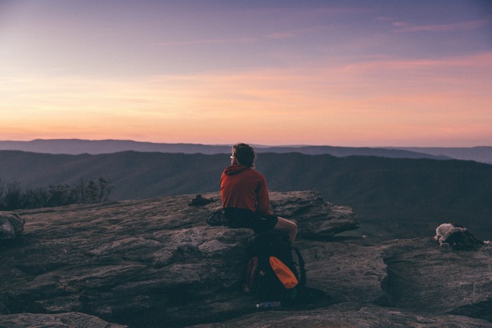 Person sitting on a mountain at sunset with a backpack