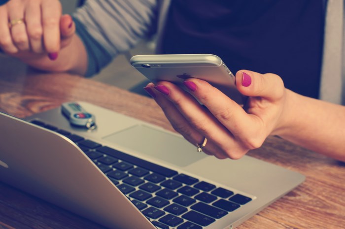 Woman using iPhone and MacBook on wooden desk