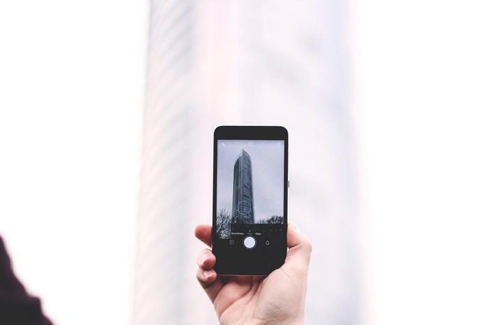 Hand holding iPhone taking a photo of a skyscraper