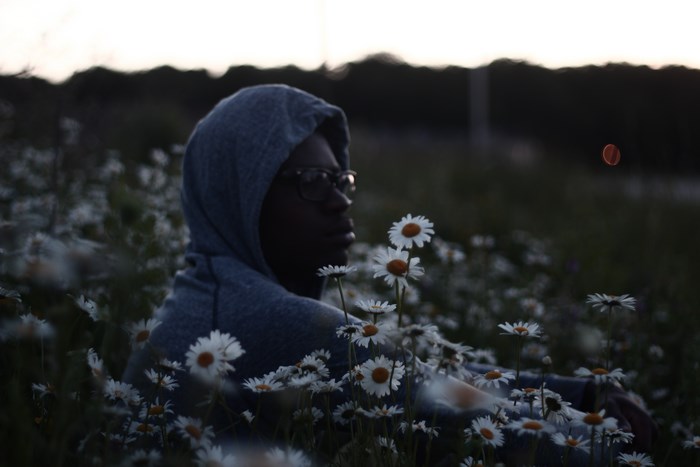 Man in hoodie sitting in a field of daisies