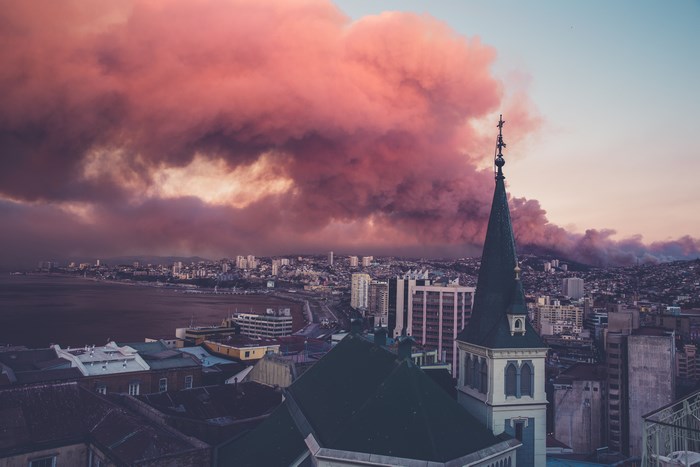 Cityscape with pink smoke and church steeple at sunset