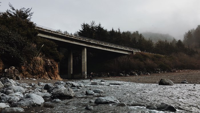 Bridge over a rocky riverbed with trees and fog