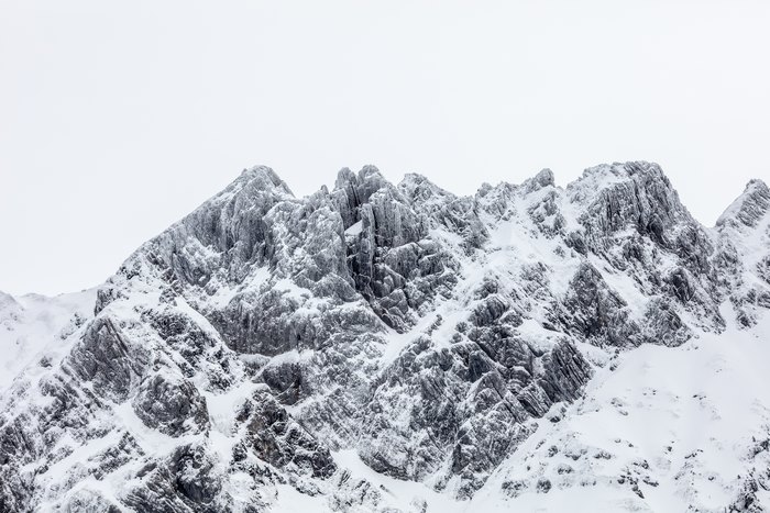 Snow-covered rocky mountain peaks under a white sky
