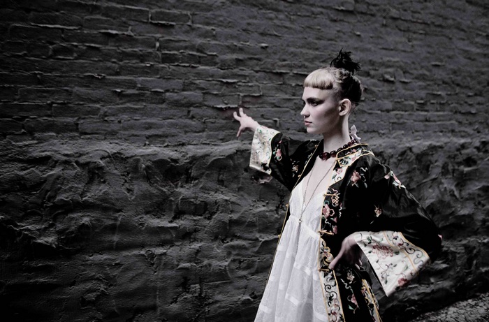 Grimes in ornate robe against brick wall