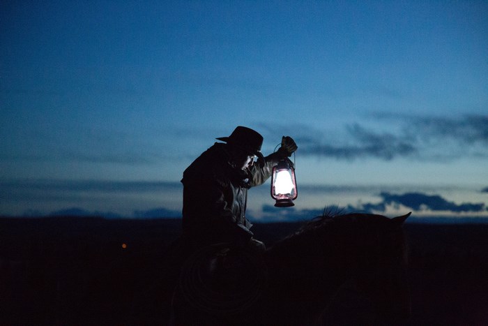 Cowboy holding a lantern on a horse at night
