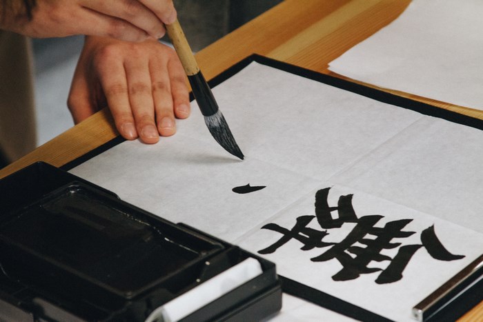 Person practicing Japanese calligraphy with brush and ink