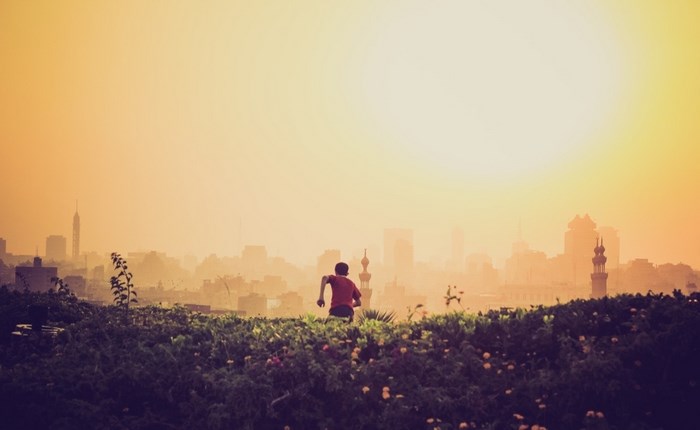 Boy running towards a hazy city skyline at sunrise