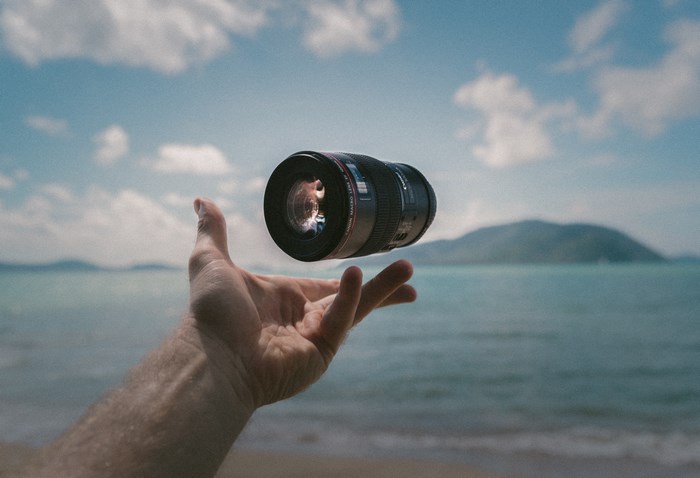 Camera lens levitating over a hand at the beach