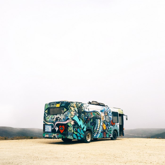 Graffiti-covered bus parked on a dirt road with hills