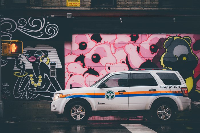 Sanitation vehicle parked in front of graffiti art