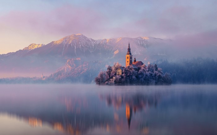 Church on island in lake with mountains and mist