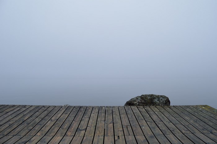 Wooden dock on a foggy lake with a rock