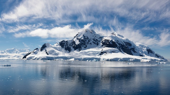 Snow-covered mountains and islands in the ocean under a cloudy sky
