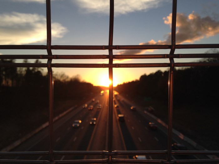Sunset over a highway seen through a fence