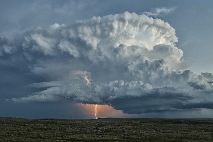 Lightning strikes a vast plain under a dramatic storm cloud formation
