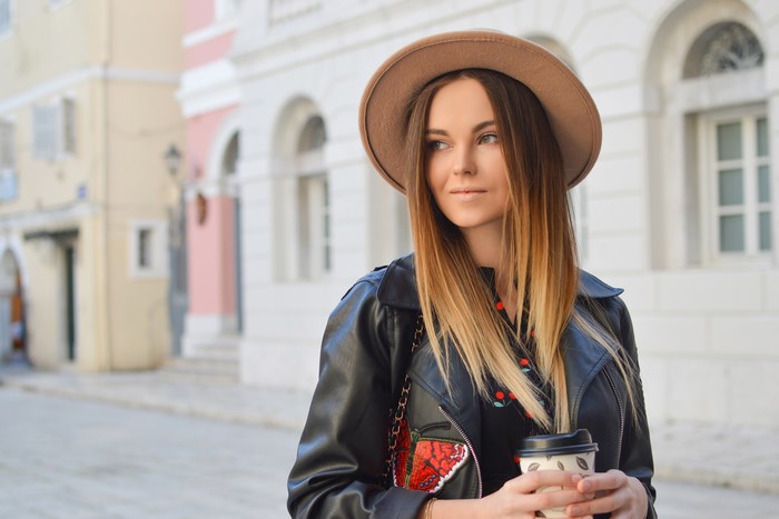 Woman in hat and leather jacket holding coffee cup in city